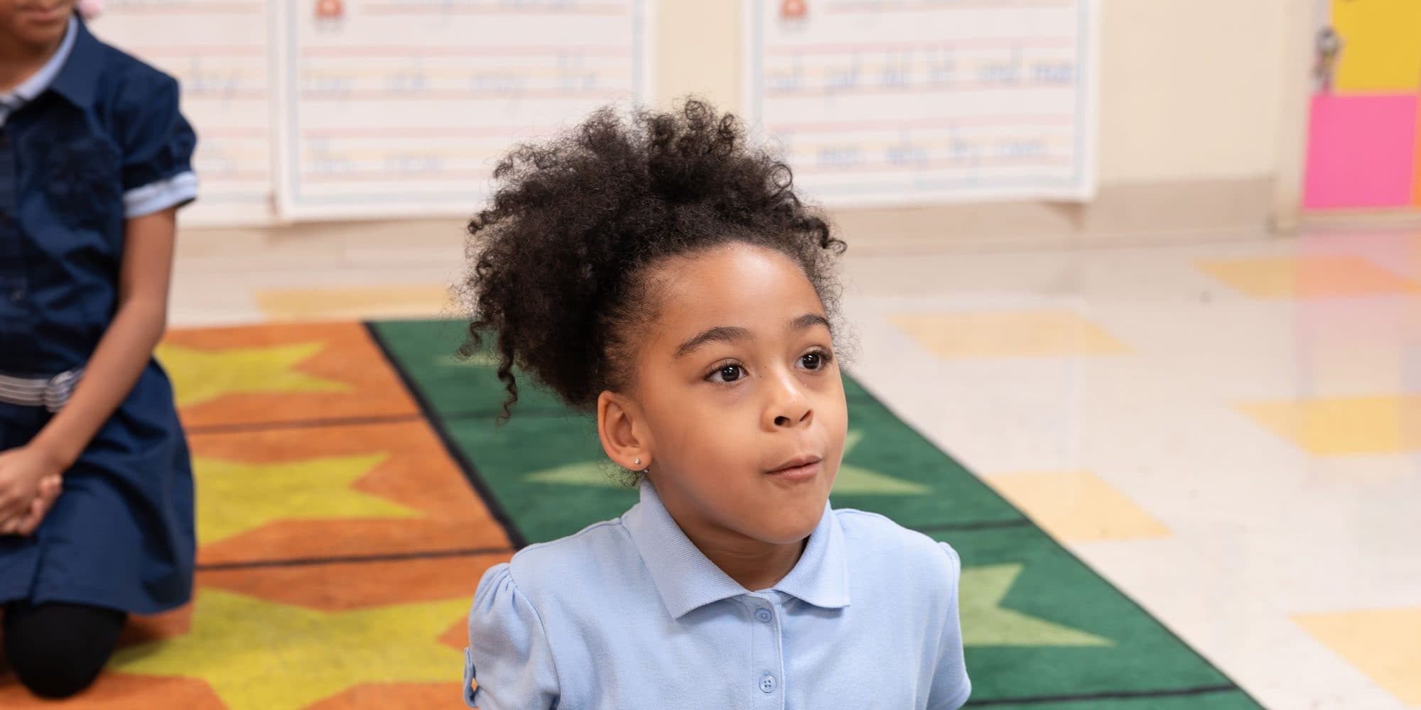Young student in a light blue polo sitting on a classroom rug.